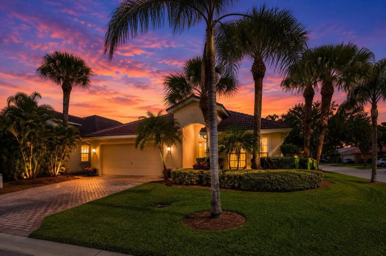 3907 Palladium View Drive at dusk — one-story tile-roof home on a corner lot with lit entry, paver driveway and palms
