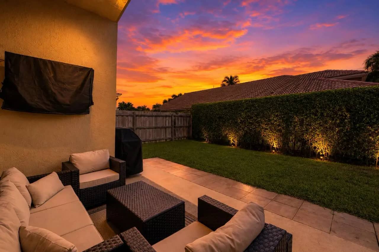 Covered patio at 3907 Palladium View Drive in the evening, with seating and uplit hedge along the fenced yard